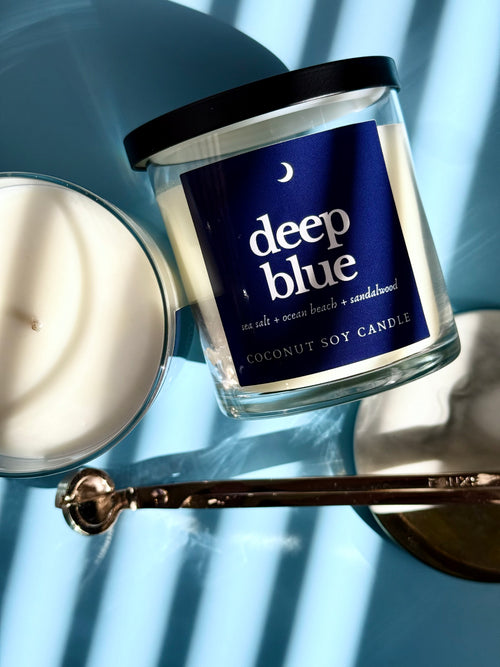 Coconut soy candle labeled 'deep blue' with a lit candle on a blue background