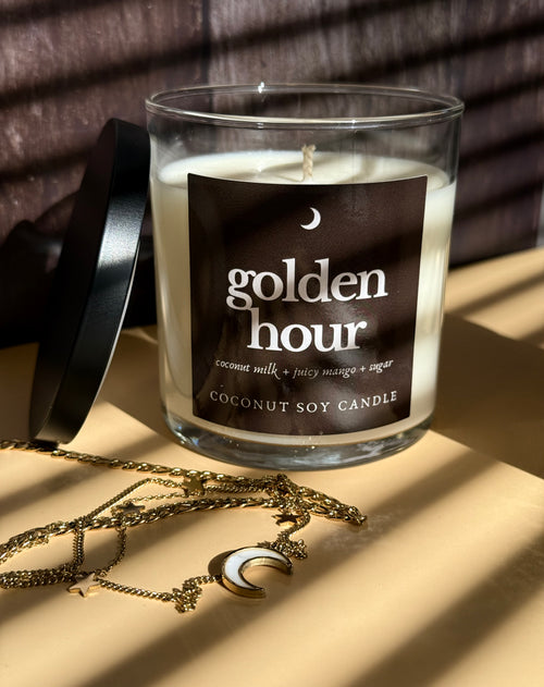 Candle labeled 'golden hour' with a necklace on a beige surface