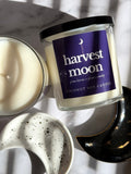 Coconut soy candle labeled 'harvest moon' on a marble surface with a blurred background