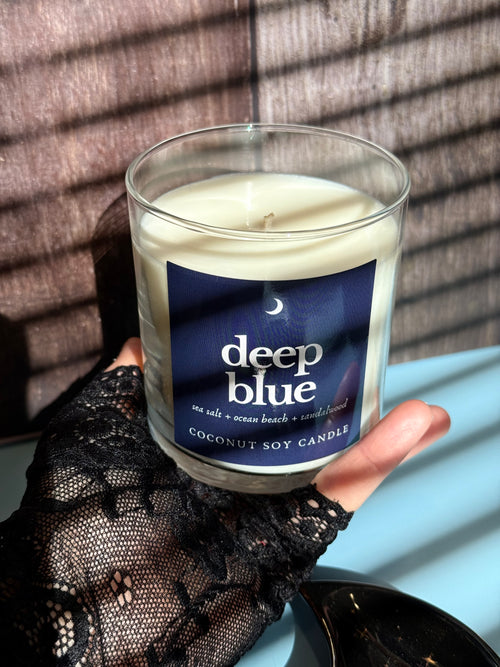Hand holding a 'deep blue' candle with a dark background