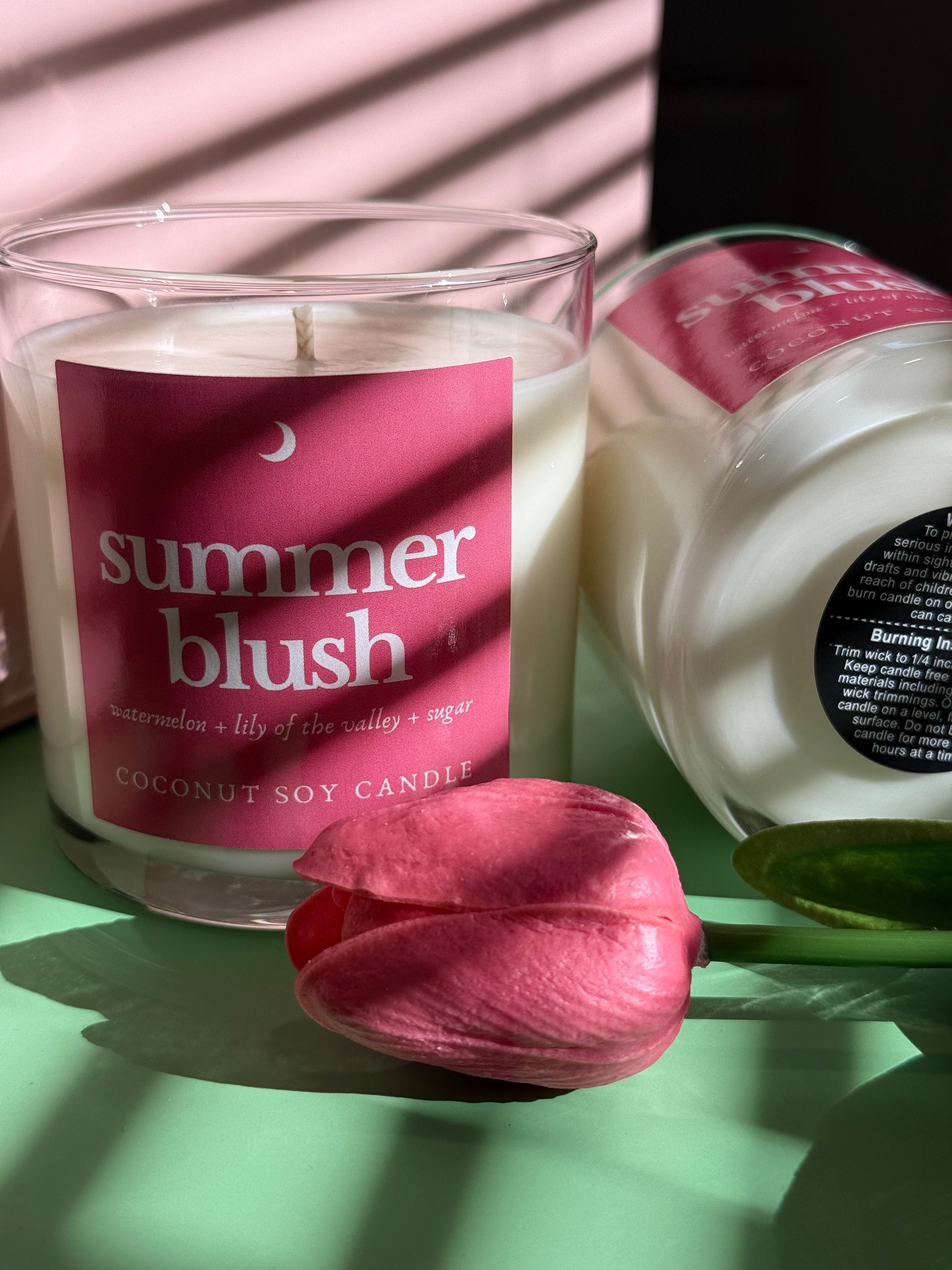 Candle labeled 'summer blush' with a pink flower on a green surface